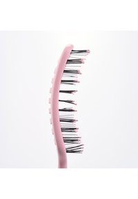 Brosse à cheveux incurvée rose avec des poils noirs flexibles surmontés de petites perles roses sur un fond blanc uni.