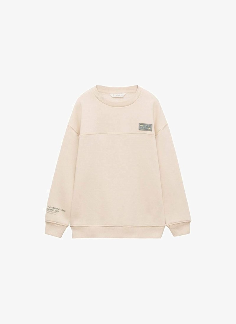 Sweatshirt beige en tissu doux, avec une couture horizontale et une petite étiquette sur la poitrine. Le texte sur la manche indique "TOUTES LES GÉNÉRATIONS CONNECTÉES."