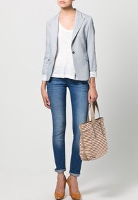 Ljusgrå randig jacka över en vit t-shirt, blå skinny jeans, bruna klackskor och en randig axelväska i beige och rosa nyanser.