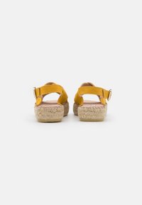 Yellow suede sandals with open backs, adjustable buckle straps, and woven jute soles. Textured surface with a natural finish on the sole.