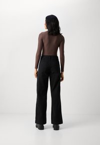 Rjava dolga majica s dolgimi rokavi, v kombinaciji z visokim pasom črnimi širokimi hlačami in močnimi črnimi platformnimi čevlji. Gladek material z oprijetim krojem.