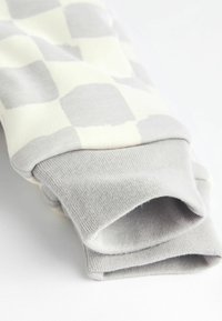 Grå og creme-rutede stof med ribbede grå manchetter; blød tekstur og afslappet design. Manchetterne er i rulle-stil for justerbar pasform.