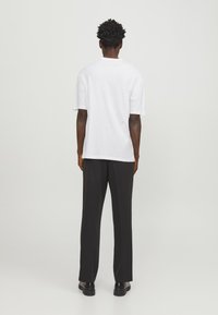Un tricou alb cu mânecă scurtă, de tip relaxat, asociat cu pantaloni negri cu picior larg. Se văd pantofi negri plat. Design simplu, fără modele sau accente.