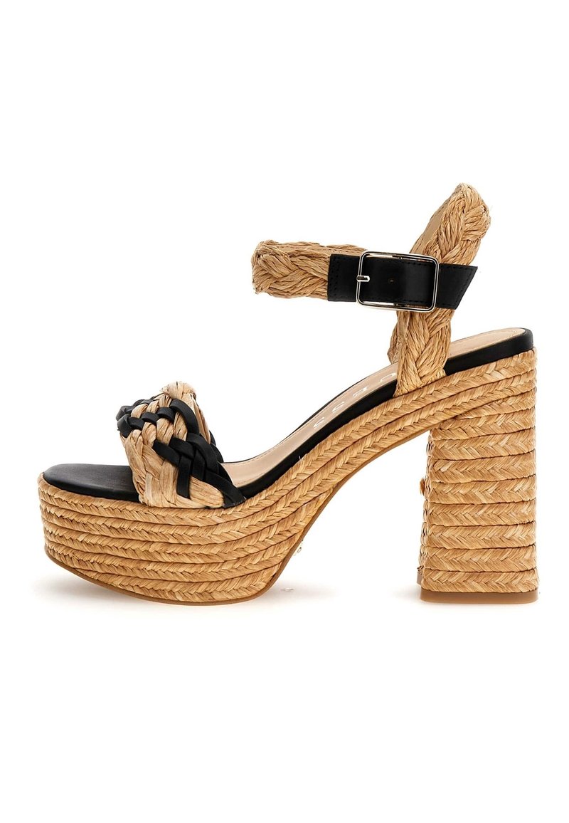 Sandale à talon en paille tissée avec une bride en cuir noir. Elle présente un talon épais et texturé de forme bloc ainsi que des détails tressés sur la partie supérieure. Couleur beige clair.