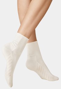 Beige Knöchelsocken mit geripptem oberen Teil, verstärkter Ferse und strukturiertem Griffmuster auf der Sohle für zusätzlichen Rutschschutz.