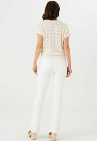 Top de punto crema con textura estampada, mangas cortas y dobladillo acanalado, combinado con pantalones blancos de campana y zapatos de plataforma tipo espadrille.