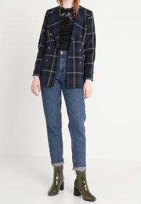 Dvouvrstvý kostkovaný blejzr ve tmavě zelené a vínové barvě, vrstvený přes černý krajkový top. Nošený s ohrnutými modrými džínami a zelenými lakovanými kotníkovými botami.