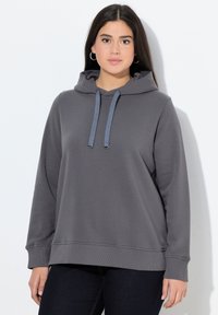 Sudadera gris con una textura suave, con cordones en la capucha, puños y dobladillo acanalados, combinada con pantalones de mezclilla oscuros.