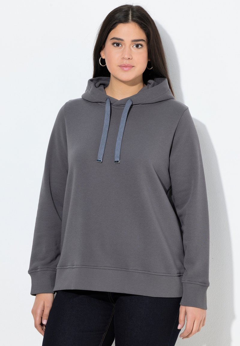 Sudadera gris con una textura suave, con cordones en la capucha, puños y dobladillo acanalados, combinada con pantalones de mezclilla oscuros.