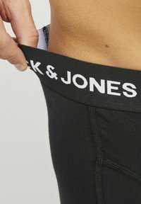 Culotte noire avec ceinture élastique portant le logo "JACK & JONES" en blanc. Vue rapprochée montrant la texture et l'élasticité du tissu.