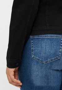Black denim jacket sleeve and blue jeans pocket with a classic V-shaped design. The jacket features button detailing and a smooth texture.