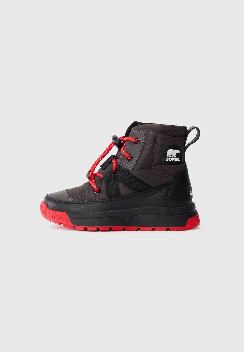 Bottine Sorel noire et rouge avec des lacets rouges, une semelle épaisse, une boucle au talon et un logo d’ours polaire sur le côté sur fond uni.
