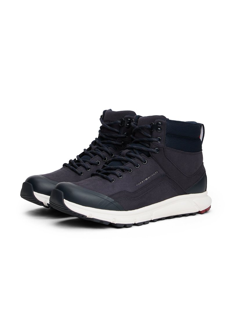 Navy mid-top sneakers made of suede and mesh with rubber toe caps, lace-up closure, and white sole with red accents.