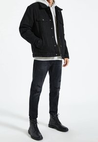 Czarna kurtka dżinsowa z kołnierzykiem, noszona na szarej bluzie z kapturem, zestawiona z przetartymi czarnymi dżinsami i czarnymi butami na sznurówki.