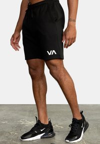Shorts neri in cotone con vita elastica e cordino, dotati di tasche laterali e di un logo bianco sulla gamba sinistra.