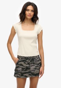 Ivoorkleurige gebreide top met een vierkante halslijn en geschulpte randen, gecombineerd met een grijze camouflageminirok met cargozakken en knoopsluiting.