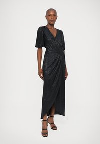 Must mustriga mustriikk Kleid, lühikeste puhvärvlitega; omadused V-kaelus, koondatud vöökoht ja kõrge lõhik. Kantud mustade rihmadega kontsadega.