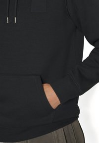 Felpa nera con tasca a marsupio, colletto con cordino, polsini a costine e un piccolo patch rettangolare del logo sul petto.