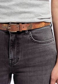 Bruine leren riem met een metalen gesp, gedragen over grijze denim jeans. De textuur is glad met een subtiel gevarieerd patroon.