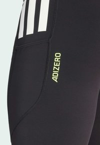 Schwarze sportliche Leggings mit glatter Textur, versehen mit weißen Streifen und einem gelben "ADIZERO"-Logo auf dem Oberschenkel. Mit einer Seitentasche.