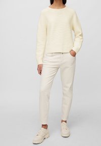 Cremfarbener Strickpullover mit rundem Ausschnitt, kombiniert mit hellbeigen, enganliegenden Jeans und beigen Sneakers mit strukturierten Sohlen.