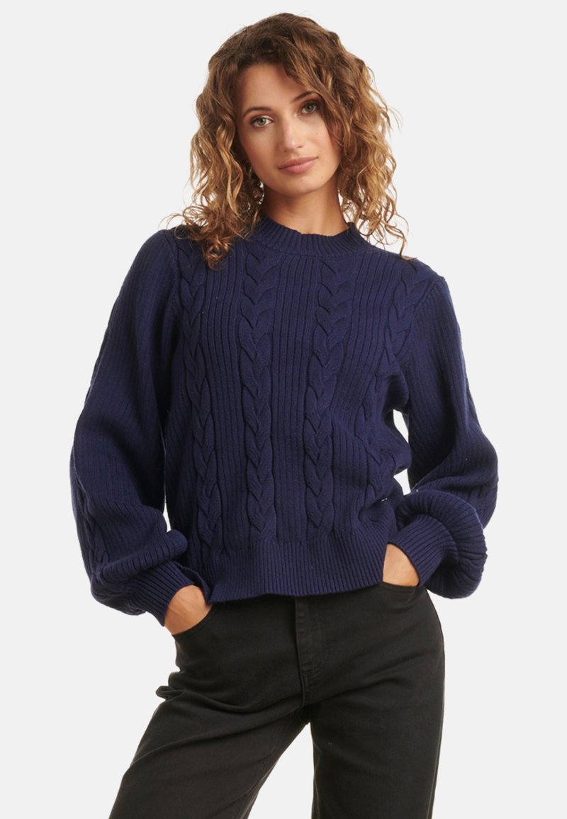 Navy blue knitted sweater featuring a ribbed design with cable knit patterns, crew neckline, and puffed sleeves, paired with black trousers.