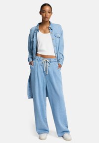 Lichtblauw denim overhemd en wijde broek. Witte crop top. Het overhemd heeft knopen en zakken; de broek heeft een trekkoord en zijzakken.