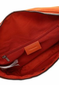 Orange fabric bag interior with a smooth texture, featuring a black zip closure, a small zip pocket, and an embossed leather tag.
