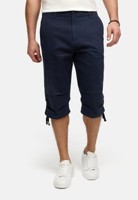 Navy cropped pants made of cotton, featuring button closure, side pockets, and adjustable drawstrings at the hem. Worn with white sneakers.