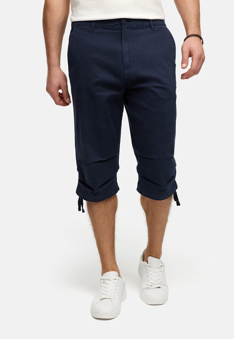 Pantalons cropped en coton navy, avec fermeture à boutons, poches latérales et cordons de serrage ajustables à l'ourlet. Portés avec des baskets blanches.