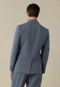 Blazer blu su misura con tessuto testurizzato, apertura singola sul retro e polsini a quattro bottoni. Design minimalista con un motivo sottile.