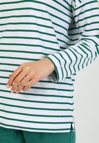 Maglione a maniche lunghe a righe verdi e bianche, con scollatura rotonda e maniche con polsini, e dettaglio con spacco laterale all'orlo.