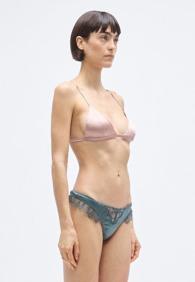 Ljusrosa satin-bh med tunna axelband, kombinerad med mörkgröna trosor med spetsdetaljer längs kanterna. Slät textur över hela plagget.