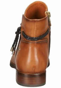 Botín de cuero marrón con detalle de cordones trenzados en negro y cremallera lateral, suela de madera y acabado suave y pulido.