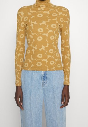 Langærmet sennepsgul rullekrave med dristigt beige blomsterprint kombineret med lyseblå højtaljede denimjeans.