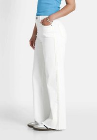 Witte wijde jeans van denim, met voorzakken, een rafelige zoom en een hoge taille, gecombineerd met grijs-witte sneakers.