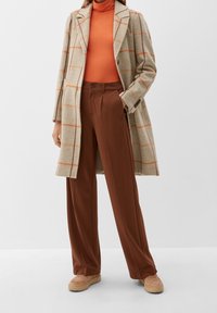 Abrigo de lana beige con cuadros naranjas, pantalones marrones de cintura alta y zapatillas beige con plataforma. Top de cuello alto en naranja brillante.