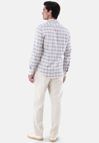 Helllila und weiße karierte Langarmbluse mit Rückenschlitz, kombiniert mit cremefarbenen Hosen und hellen Schuhen.