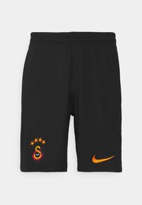 Short de sport noir avec taille élastique, arborant un blason multicolore de Galatasaray à gauche et un logo Nike orange à droite.