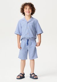 Chemise à manches courtes à carreaux et shorts assortis en tissu bleu et blanc, avec une fermeture à boutons et une taille élastique avec cordon de serrage.