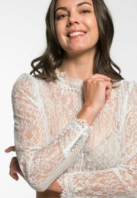 Kanten blouse met lange mouwen, intricare bloemenpatronen en een hoge halslijn. Verfraaid met parelknoopjes op de manchetten. Kleur: wit.