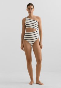 Egyrészes fürdőruha egy vállpánttal, vízszintes tengerészkék és krémszínű csíkokkal, struktúrált anyagból, magasan kivágott lábakkal és derékvágással.