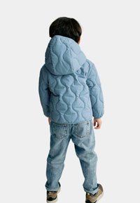 Kvadra-blå huvjacka med ett vågigt mönster, parat med ljusblå jeans och sneakers. Jackan har en avslappnad passform och en slät textur.