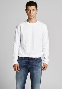 Witte langafslank T-shirt gemaakt van katoen, gecombineerd met blauwe denim jeans. T-shirt heeft een ronde halslijn en een losse pasvorm; de jeans hebben een vervaagde afwerking.