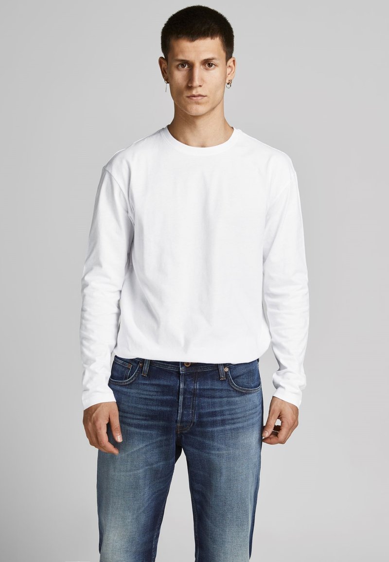 Witte langafslank T-shirt gemaakt van katoen, gecombineerd met blauwe denim jeans. T-shirt heeft een ronde halslijn en een losse pasvorm; de jeans hebben een vervaagde afwerking.