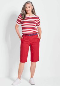 Rote Leinen-Bermudashorts mit Seitentaschen, kombiniert mit einem gestreiften Oberteil in Rot, Weiß und Blau aus Strick. Dazu werden weiße Sneakers getragen.