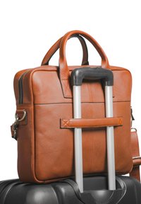 Mallette en cuir marron avec deux poignées, forme rectangulaire et texture lisse, attachée à une valise noire avec une poignée télescopique.