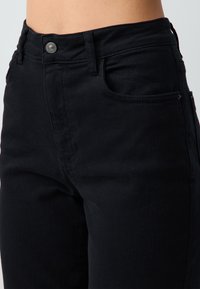 Jeans neri a vita alta in denim, con una vestibilità classica, cuciture sottili e una chiusura con bottone metallico in vita.