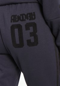 Námořnické teplákové kalhoty s velkým černým potiskem "03" a texturovanými akcenty. Tkanina má měkkou, hladkou texturu a boční pruhy.