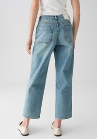 Lichtblauwe, high-waisted jeans met een relaxed fit. Beschikt over twee rechthoekige achterzakken en zichtbare stiksels. G gedragen met beige instappers.